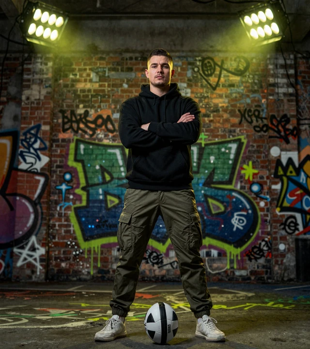 Street-Football-Spieler in Streetwear vor einer Graffiti-Wand mit Neonscheinwerfern bei Golisimo Casino
